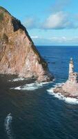 Top view of dramatic landscape of rocky island and lighthouse in sea. Clip. Cinematic fairy-tale landscape of rocky cape and lighthouse in ocean. Magical landscape of rocks and abandoned lighthouse in video