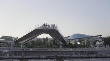 Beautiful bending bridge above river on a blue sky background. Action. Many tourists on the bridge on a summer day. video
