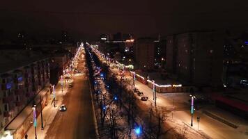 View of the night year from a helicopter. Clip. A dark city illuminated by street lamps with high houses and towers and a road with traffic is visible. video