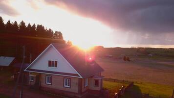 Beautiful dawn sun shines on rustic landscape in summer. Clip. House in village on background of bright dawn sun. Rustic summer landscape with house and dawn rays of red sun and gray clouds video