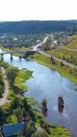 Top view of village and old bridge over river. Clip. Beautiful landscape of village on river with bridge in summer. Stone bridge across river in forest area with village video