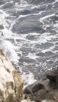Close-up of grey waves with foam breaking on the rocks in the sea. Action. View to the sea from rock. video