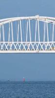 Breathtaking seascape with a white beautiful bridge with many moving cars above the water surface and sailing ships, time lapse effect. Shot. Calm sea with ripples, huge bridge, vessel and bue sky. video