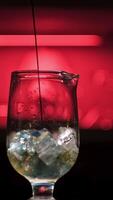 Pouring fresh alcoholic drink into the glass with ice cubes on the bar counter. Stock footage. Close up of process of cocktail preparation, adding blue syrup into the glass. video