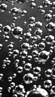 Abstract air bubbles moving underwater. Stock footage. Close up of round transparent oxygen bubbles flowing slowly isolated on black background, monochrome. video