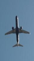 View from the bottom on a large white passenger plane flying against the clear blue sky. Action. Flight to the summer resort. video