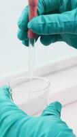 Close up of transparent liquid being poured into a bottle with a pipette on a white background. Clip. Hands in gloves pressing on a pipette. video