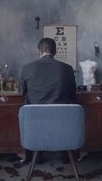 Young man in black shirt sitting in comfortable chair and working at the table in entourage art workshop. Stock footage. Freelancer working at home, view from back video