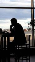 Businessman waiting for boarding at the airport and looking through panoramic windows. Silhouette of a man at a table. video