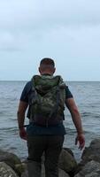 Man walks on stone coast on background of sea. Clip. Man walks on stones of sea embankment on cloudy day. Walk along sea stone coast on cloudy day video