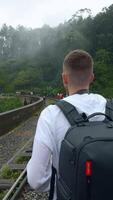 Rear view of a man tourist taking pictures of mountain forested landscape on smartphone. Action. Hiker walking on railways. video