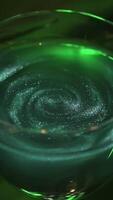 Wine glass with green coctail on dark green background with plant leaves. Stock footage. Close up of alcoholic beverage of green color with shining particles. video