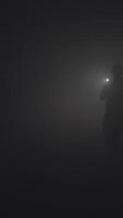 Silhouette of man in thick fog. Stock footage. Black silhouette of man with flashlight shining in thick grey smoke. Man with flashlight makes his way through darkness in smoke video