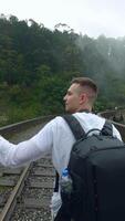 Rear view of a man tourist taking pictures of mountain forested landscape on smartphone. Action. Hiker walking on railways. video