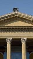 Facade of ancient building with columns and triangular portico. Action. Beautiful historical building with antique architecture and columns on blue sky background video