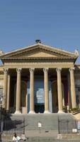 Facade of ancient building with columns and triangular portico. Action. Beautiful historical building with antique architecture and columns on blue sky background video