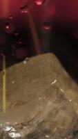 Pouring fresh alcoholic drink into the glass with ice cubes on dark background with red dim light. Stock footage. Close up of process of cocktail preparation, adding beverage into the glass. video