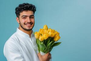 Smiling man holding a bouquet of yellow tulips against a bright blue background indoors photo