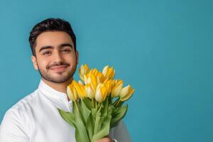 Smiling man holding a bouquet of yellow tulips against a bright blue background indoors photo