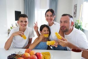 Family enjoying corn on the cob at a cozy dining table in a bright, modern home photo