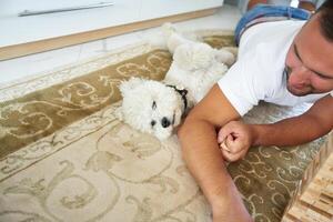Man relaxing on carpet with a white dog in a cozy indoor setting during the day photo