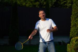 Man playing badminton outdoors in a garden during late afternoon photo