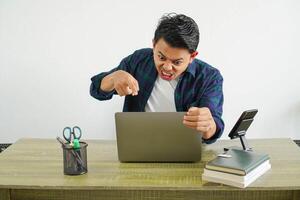 young asian man in a workplace very angry while pointing at the laptop screen on white background photo