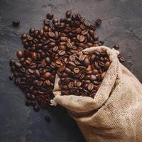 Dark brown coffee beans being poured out of a sack on a wooden background. This image conveys the freshness and aroma of the coffee beans. photo