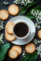 Coffee and cookies surrounded by fresh lily of the valley flowers on a blue textured surface photo