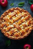 Homemade apple pie with a golden lattice crust on a dark surface surrounded by fresh apples photo