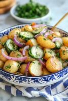 Fresh herb potato salad served in a decorative bowl with red onions and cucumbers photo