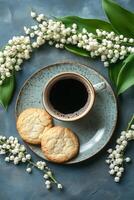 Coffee and cookies surrounded by fresh lily of the valley flowers on a blue textured surface photo