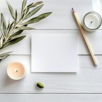 A tranquil workspace with candles, fresh greenery, and blank paper on a wooden table photo