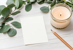 A cozy arrangement featuring a candle, greenery, and a blank card on a rustic table photo
