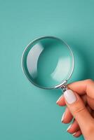 Hand holding a magnifying glass over a turquoise background for detailed examination photo