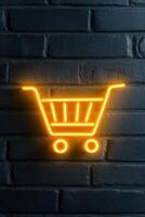 Neon shopping cart emblem glowing on a textured brick wall in an urban setting photo