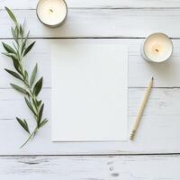 A tranquil workspace with candles, fresh greenery, and blank paper on a wooden table photo