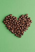 Heart-shaped arrangement of coffee beans on a green background showcasing love for coffee photo