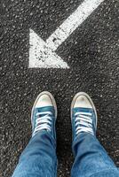 Feet in turquoise shoes standing on asphalt by a white directional arrow pointing forward photo