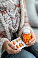 Elderly person holding a bottle of medication and a blister pack while sitting at home photo