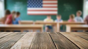 Wooden tabletop in a classroom with chalkboard and American flag in the background photo