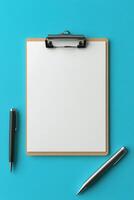A blank clipboard and pens resting on a vibrant turquoise background for creative tasks photo