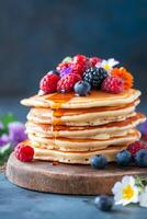 Delicious stack of pancakes topped with fresh berries and syrup on a wooden board photo