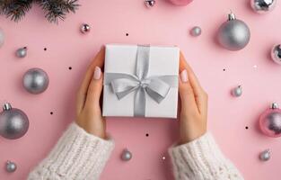 Christmas gift wrapping with silver accents surrounded by ornaments on a pink background photo