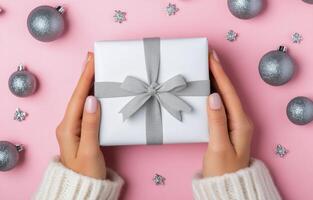 Christmas gift wrapping with silver accents surrounded by ornaments on a pink background photo