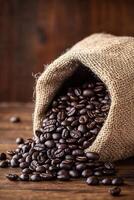 Freshly roasted coffee beans spilling from a burlap sack on rustic wooden surface photo