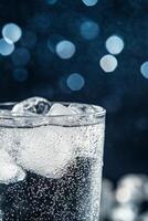 A refreshing glass of sparkling water with ice cubes on a dark background photo
