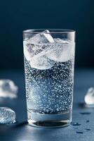 A refreshing glass of sparkling water with ice cubes on a dark background photo