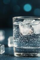 A refreshing glass of sparkling water with ice cubes on a dark background photo