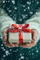 A person holds a beautifully wrapped gift with a red bow while snow falls gently around them photo